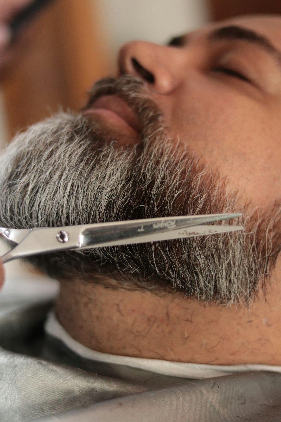 Barber uses silver shears to trim a man's beard.
